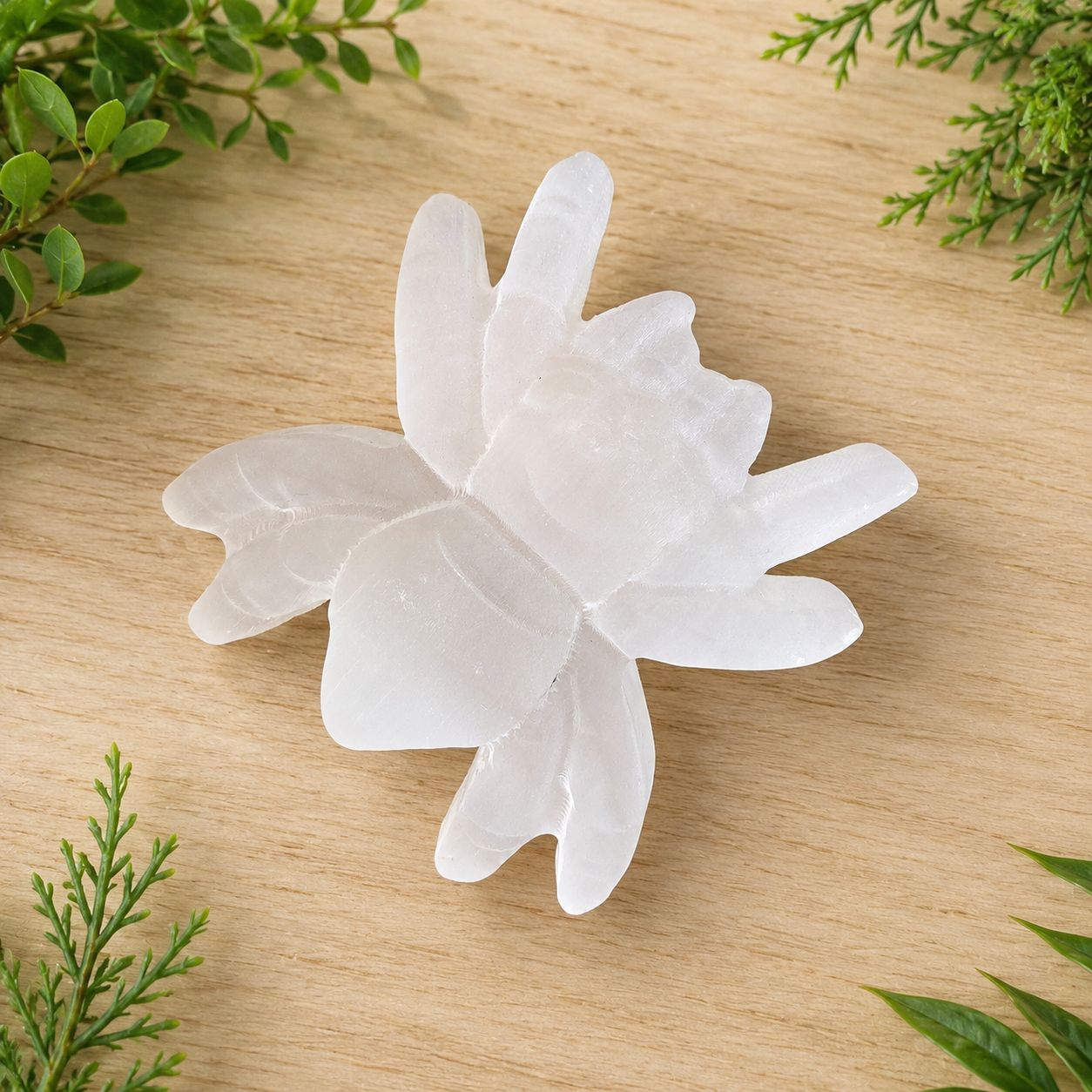 Selenite spider carving on light wooden table with greenery