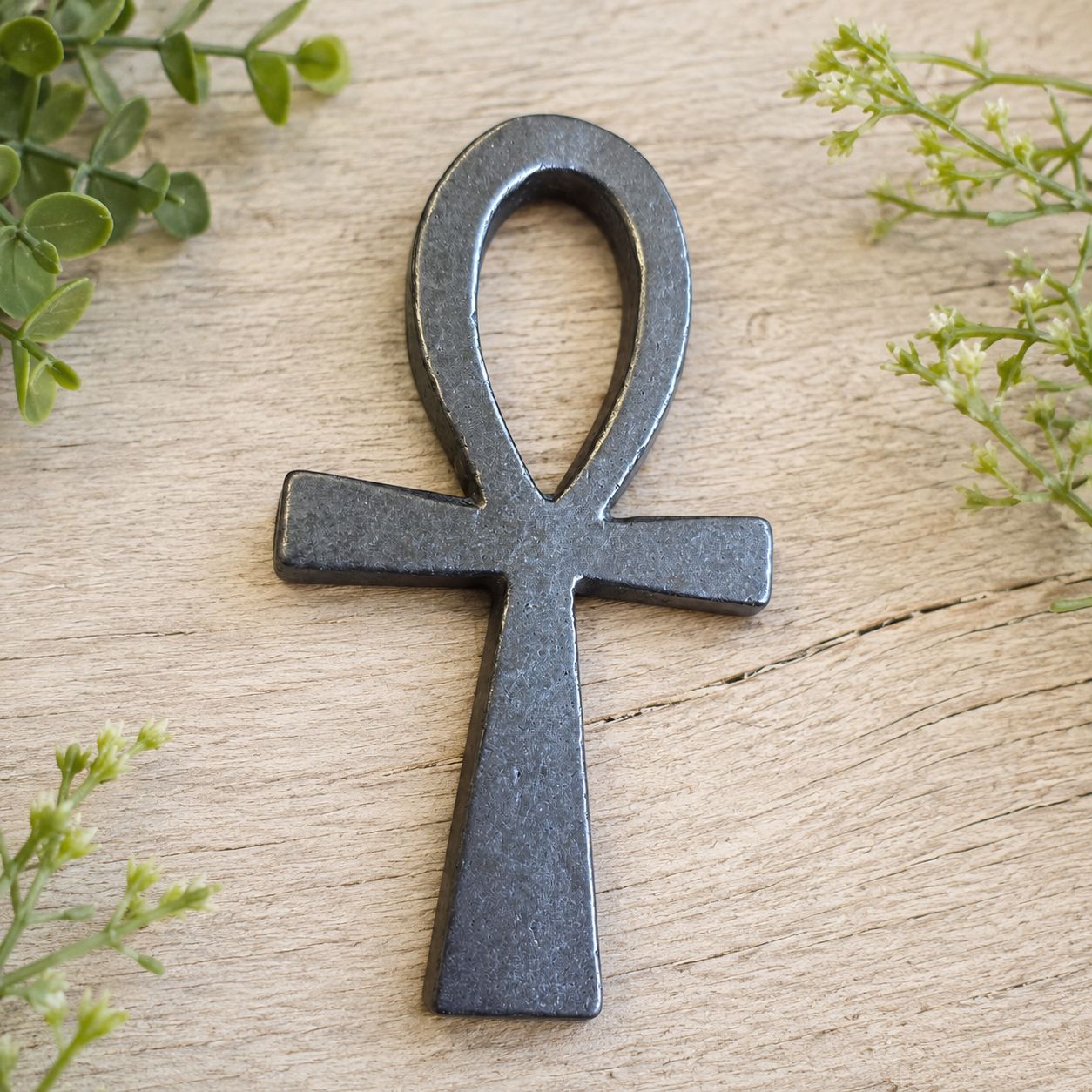Shungite Ankh carving on light wooden table with greenery