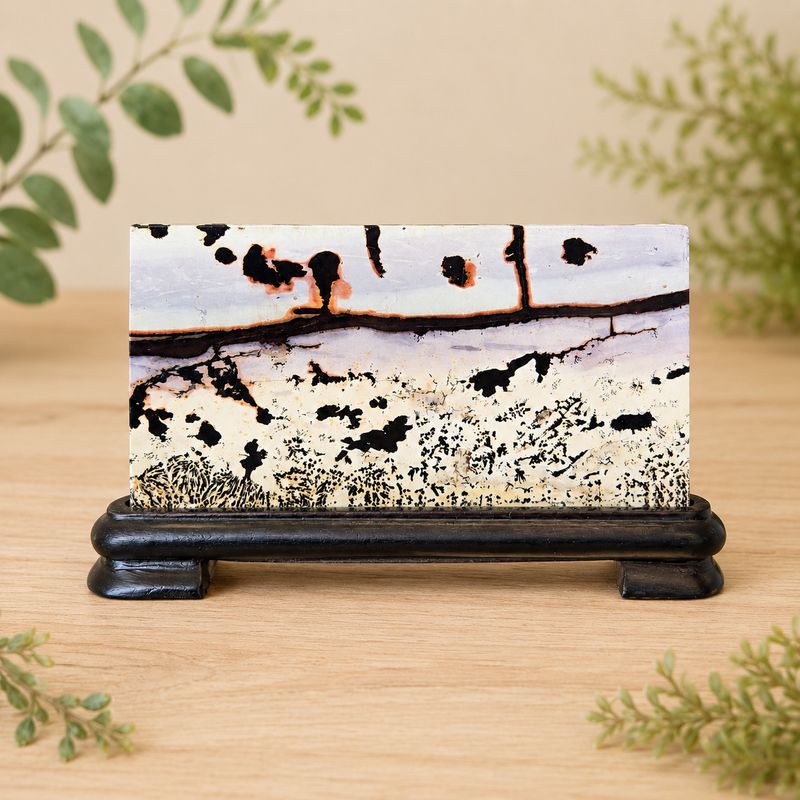 Front of small picture jasper rectangle slab with wooden stand on light wooden table with greenery.