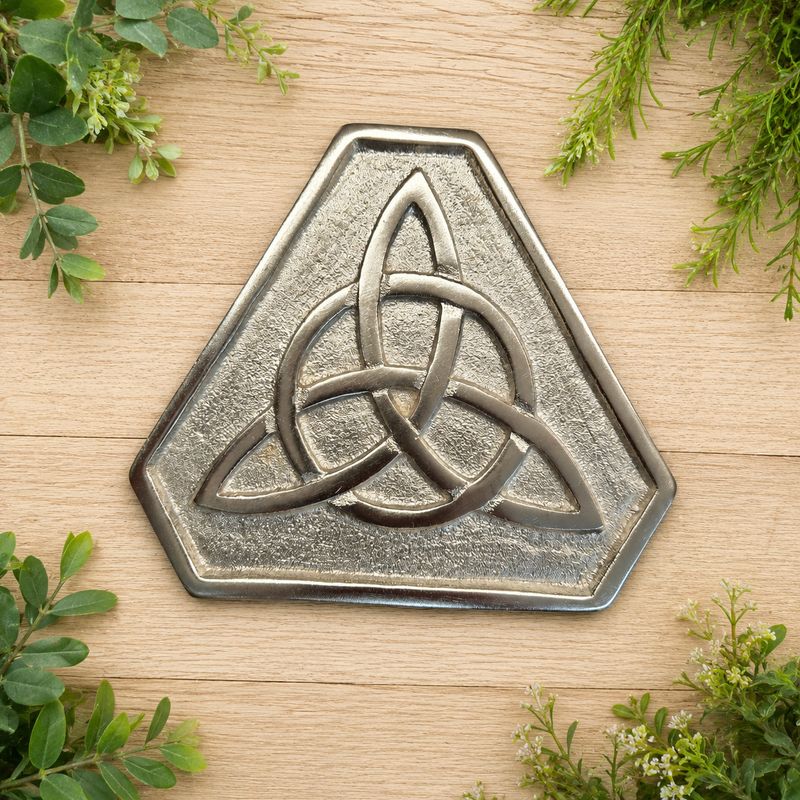 Silver aluminum Triquetra altar tile displayed on a light wooden table with greenery.