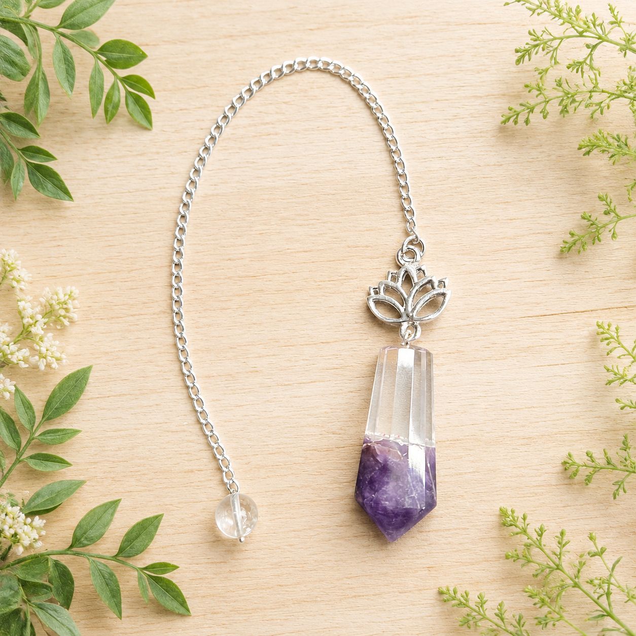 Amethyst and quartz lotus pendulum on light wood with greenery.