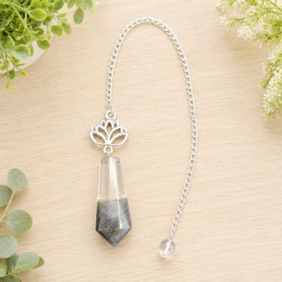 Labradorite and quartz lotus pendulum on light wood with greenery.
