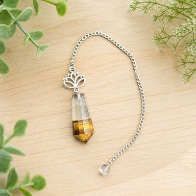Tiger eye and quartz lotus pendulum on light wood with greenery.