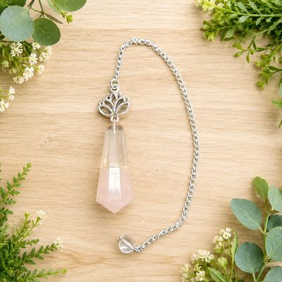 Rose quartz and quartz lotus pendulum on light wood with greenery.