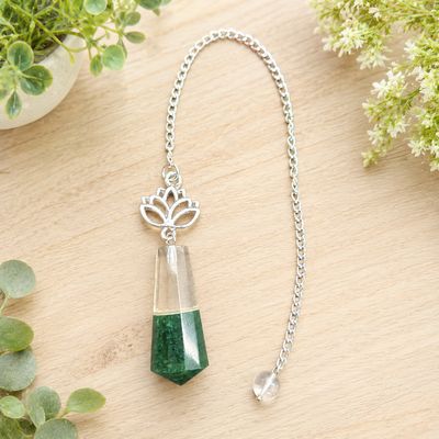 Green aventurine and quartz lotus pendulum on light wood with greenery.