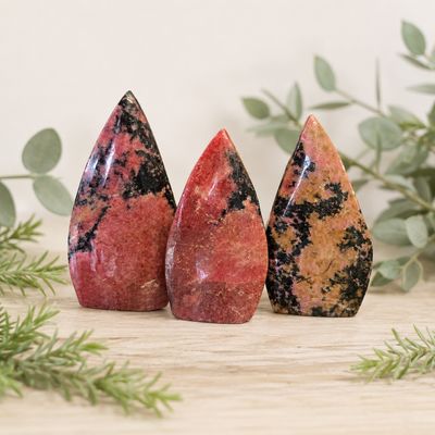 Rhodonite arrow shapes at Arkady’s Metaphysical Gifts displayed on a light wooden table with greenery