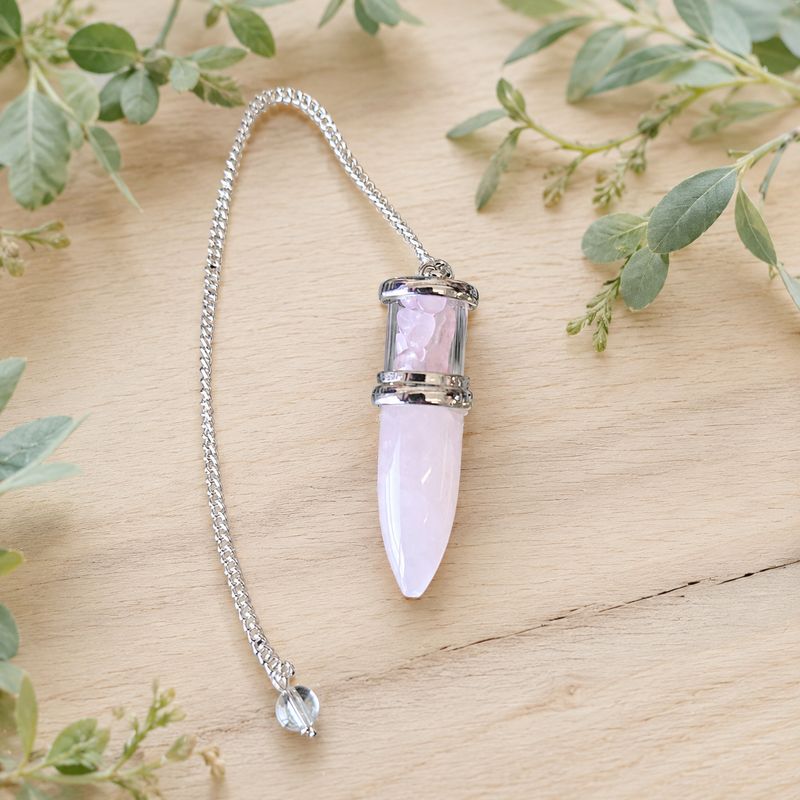 Rose Quartz Bullet Chips Pendulum with silver-toned chain and clear bead on a light wooden table