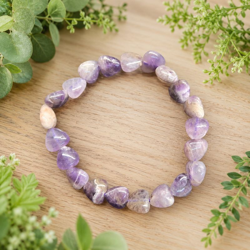 Dream amethyst heart bracelet displayed on a light wooden table with greenery.