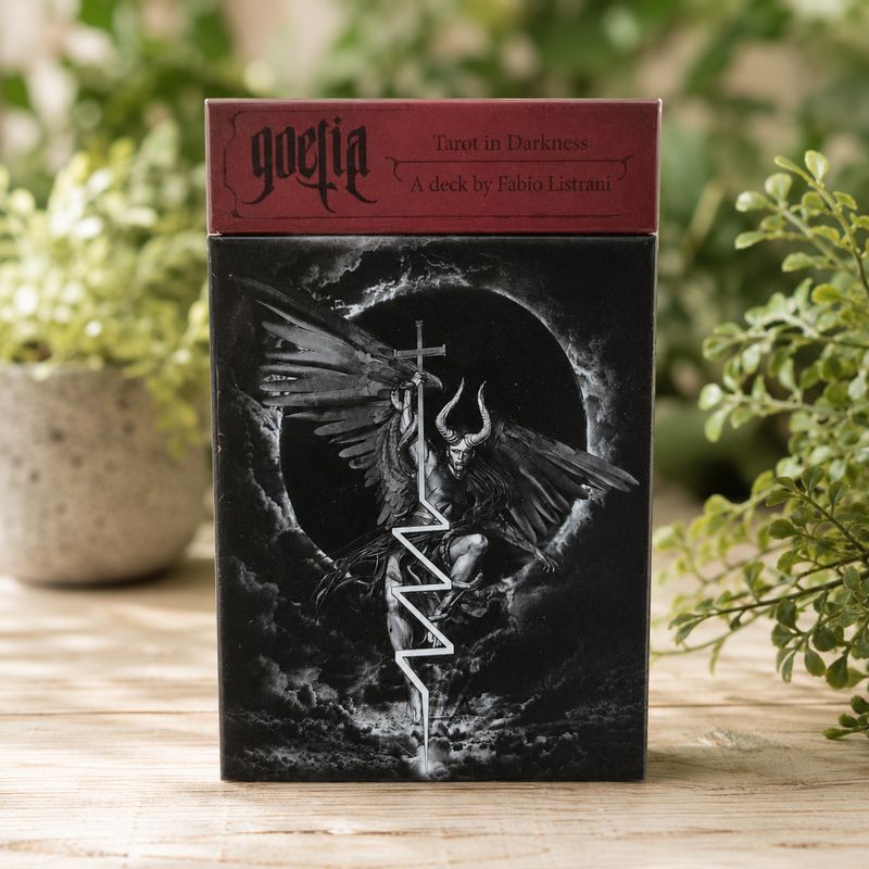 Front of Goetia Tarot in Darkness by Fabio Listrani displayed on a light wooden table with greenery