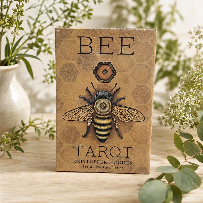 Bee Tarot deck by Kristoffer Hughes with honeybee artwork displayed on a light wooden table with greenery