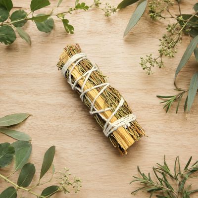 Rosemary and Palo Santo smudge stick on a light wooden table with greenery