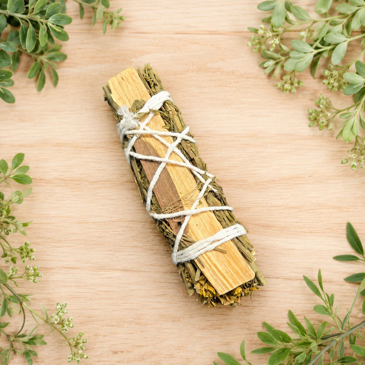Rue and Palo Santo smudge stick displayed on a light wooden table with greenery
