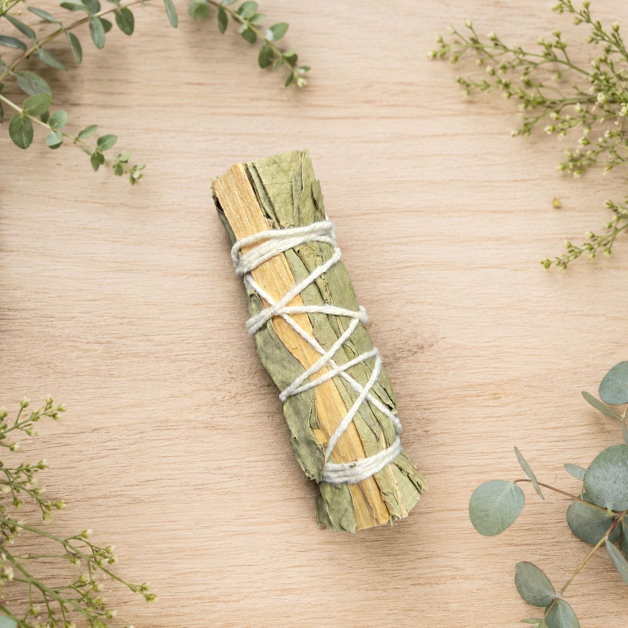 Eucalyptus and Palo Santo smudge stick displayed on a light wooden table with greenery