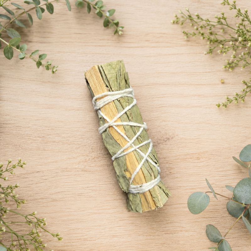 Eucalyptus and Palo Santo smudge stick displayed on a light wooden table with greenery