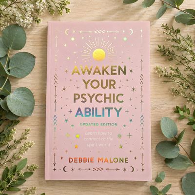 Awaken Your Psychic Ability by Debbie Malone on a light wooden table with greenery.