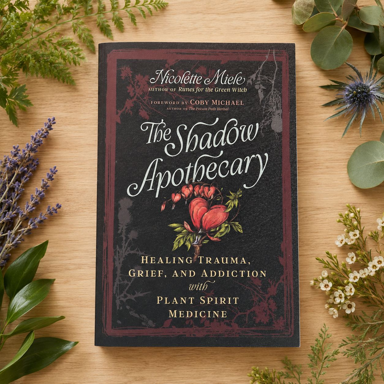 The Shadow Apothecary by Nicolette Miele displayed on a light wooden table with greenery.
