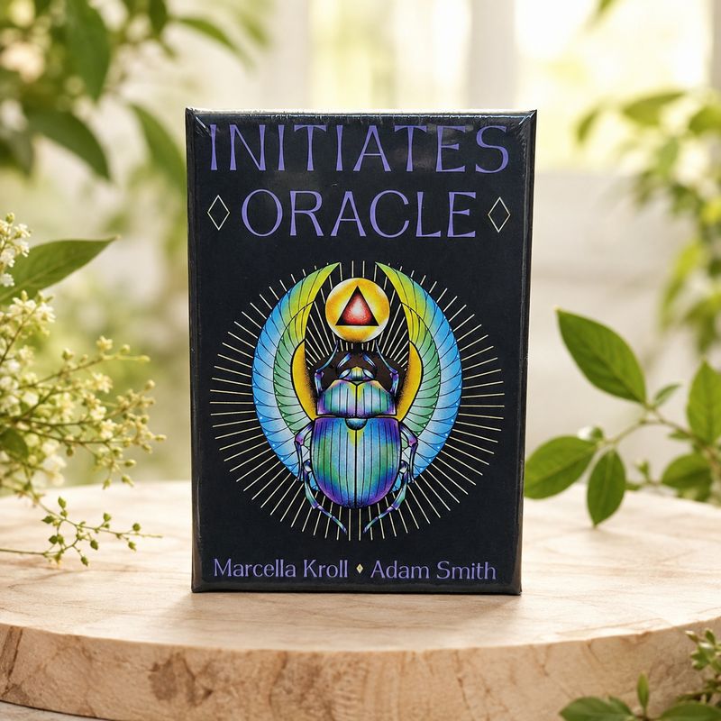 Initiates Oracle deck with colorful scarab artwork displayed on a light wooden table with greenery.