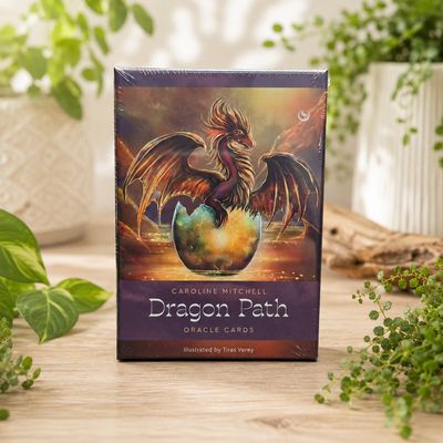 Dragon Path Oracle Cards box featuring a winged dragon emerging from a glowing egg on a light wooden table.