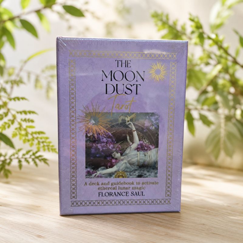 The Moon Dust Tarot deck by Florance Saul displayed on a light wooden table with soft greenery.