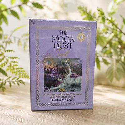 The Moon Dust Tarot deck by Florance Saul displayed on a light wooden table with soft greenery.