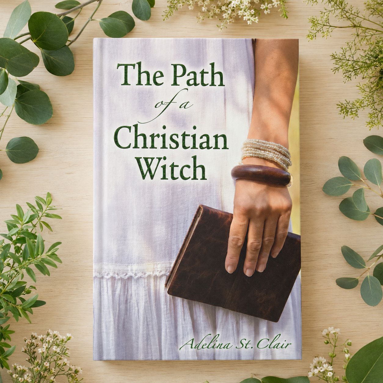 The Path of a Christian Witch by Adelina St. Clair on a light wooden table with greenery.