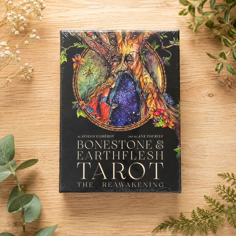 Bonestone &amp; Earthflesh Tarot deck displayed on a light wooden table with greenery.