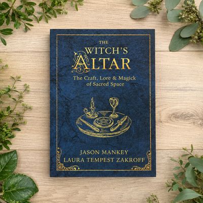 The Witch’s Altar book by Jason Mankey and Laura Tempest Zakroff on a light wooden table with greenery.