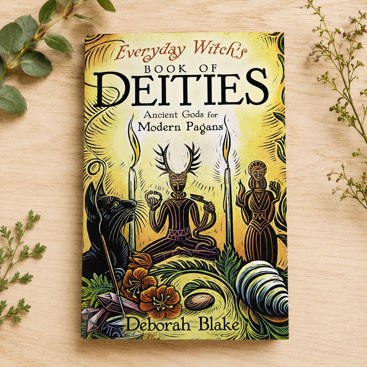 Everyday Witch’s Book of Deities by Deborah Blake on a light wooden table with greenery.