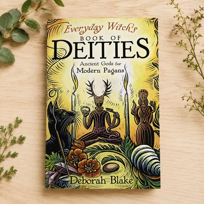 Everyday Witch’s Book of Deities by Deborah Blake on a light wooden table with greenery.