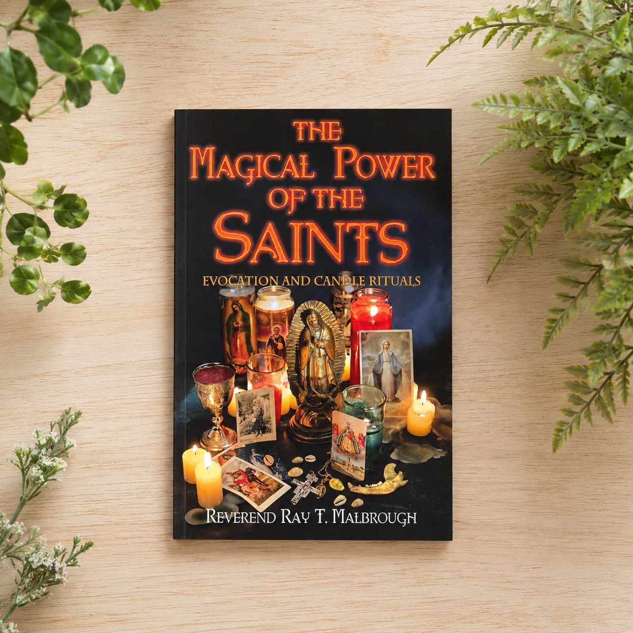 The Magical Power of the Saints by Ray T. Malbrough on a light wooden table with greenery.