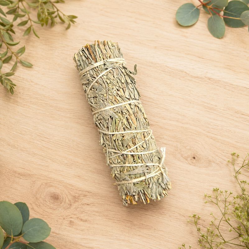 Blue sage smudge on a light wooden table with greenery