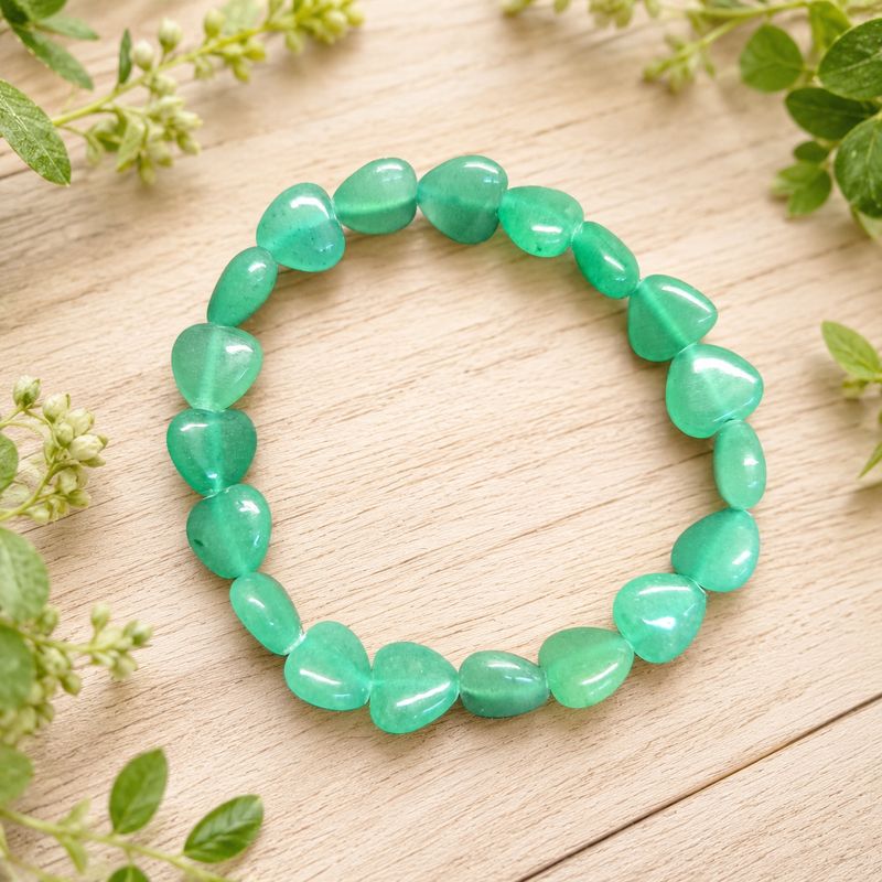 Green aventurine heart bracelet displayed on a light wooden table with greenery.