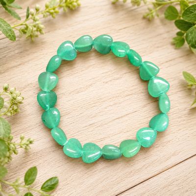 Green aventurine heart bracelet displayed on a light wooden table with greenery.