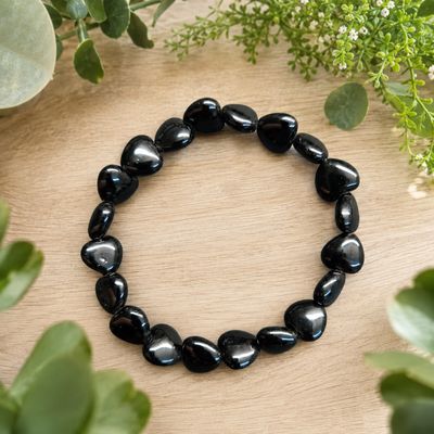 Black obsidian heart bracelet displayed on a light wooden table with greenery.