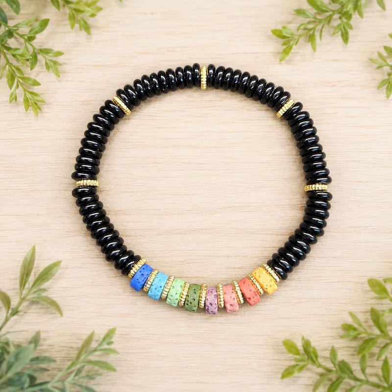 Chakra volcanic rock Obsidian bracelet with colorful beads on a light wooden table with greenery.