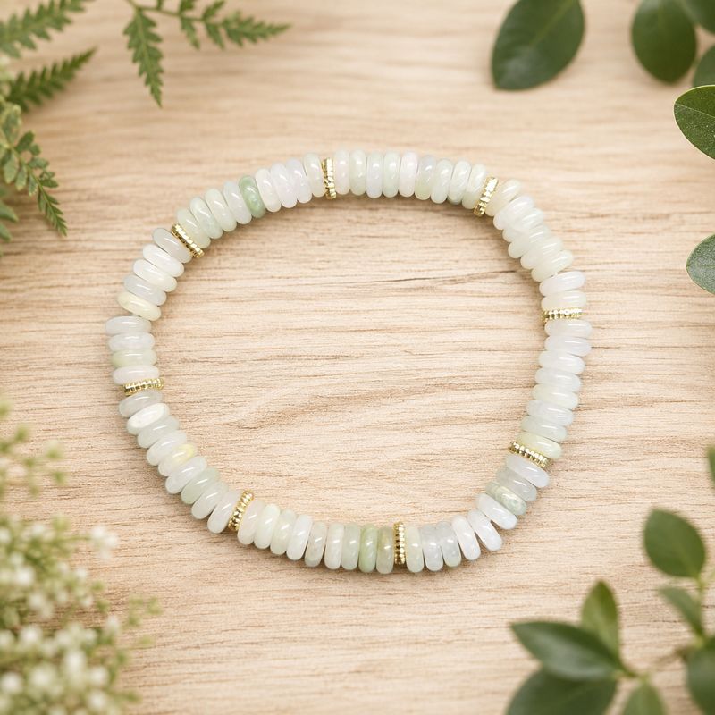 Tianshan Jade disc bracelet with gold accents on a light wooden table with greenery.
