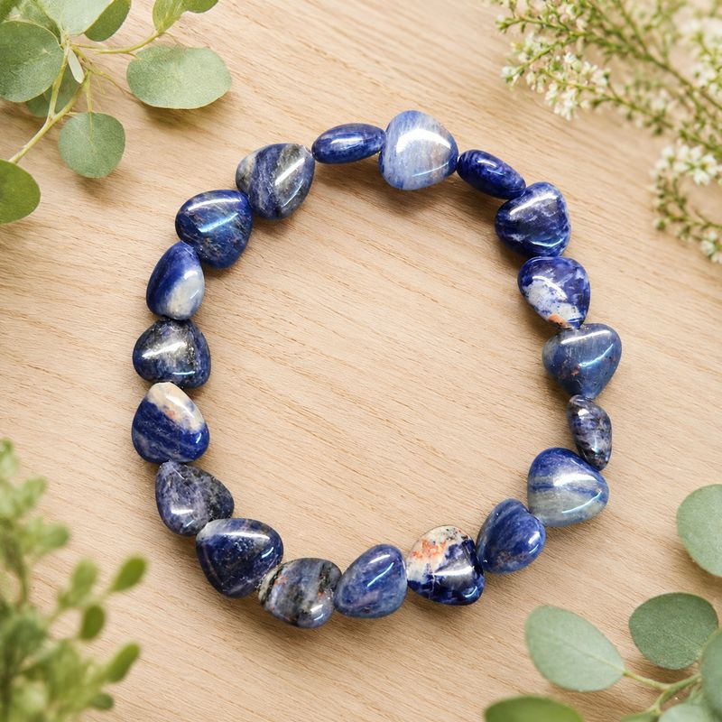 Sodalite heart bracelet displayed on a light wooden table with greenery.