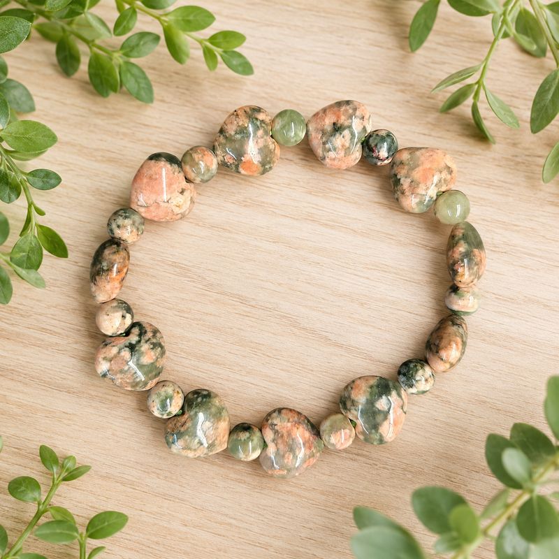 Green Rutile Flower Agate heart bracelet on a light wooden table with greenery.