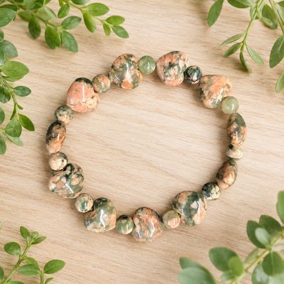 Green Rutile Flower Agate heart bracelet on a light wooden table with greenery.