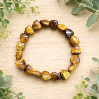 Tiger eye heart bracelet displayed on a light wooden table with greenery.