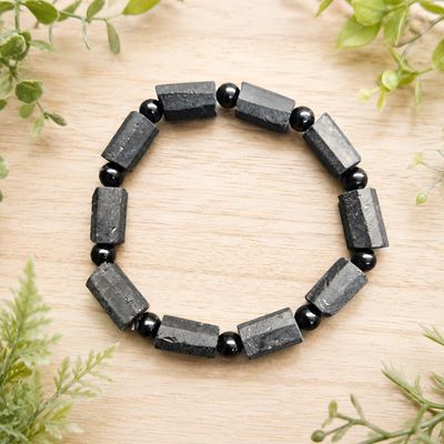Raw black tourmaline and bead bracelet displayed on a light wooden table with greenery.