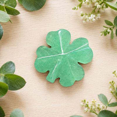 Polished Green Aventurine Lucky Clover carving displayed on a light wooden table with greenery.