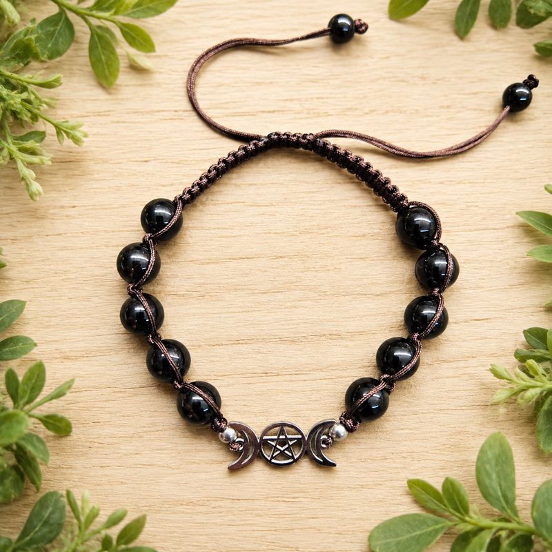 Triple Moon Pentagram Obsidian adjustable bracelet on a light wooden table with greenery.