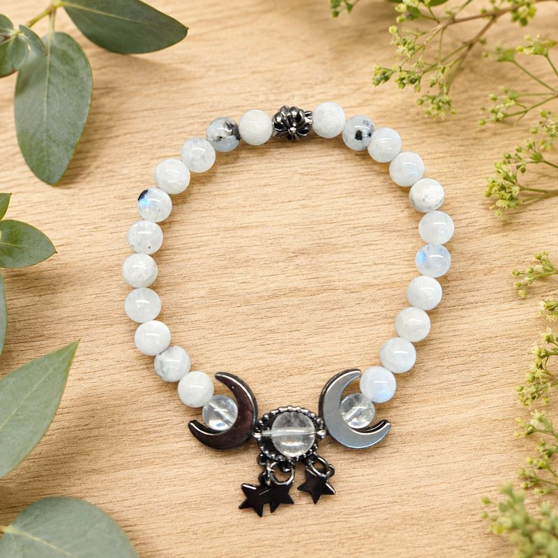 Rainbow Moonstone Quartz bracelet with crescent moon and star charms on a light wooden table.