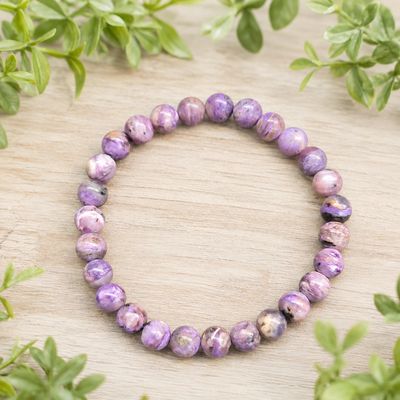 Charoite 7mm gemstone bracelet displayed on a light wooden table with greenery.