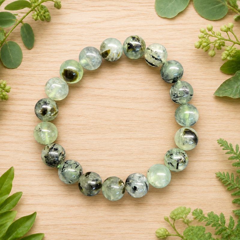 Prehnite with Epidote 10mm gemstone bracelet on a light wooden table with greenery.