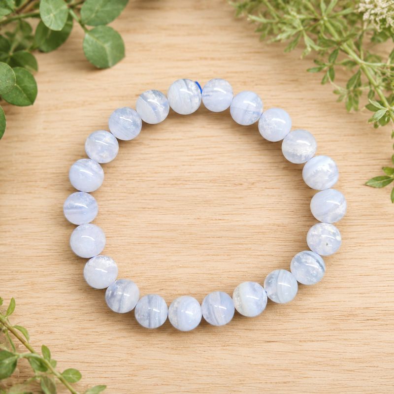 Blue Lace Agate 8mm bead bracelet displayed on a light wooden table with greenery.