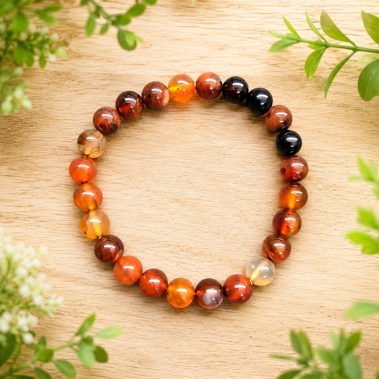 Sardonyx 8mm bracelet with warm red, orange, brown, and black beads on a light wooden table with greenery.
