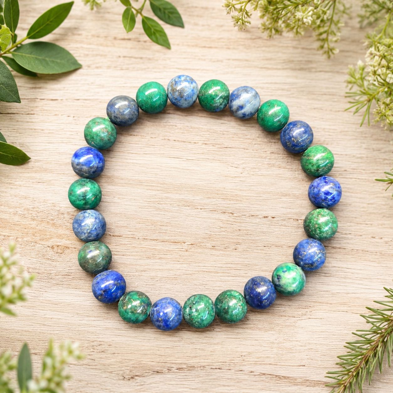 Azurite 8mm bracelet with blue and green beads on a light wooden table with greenery.