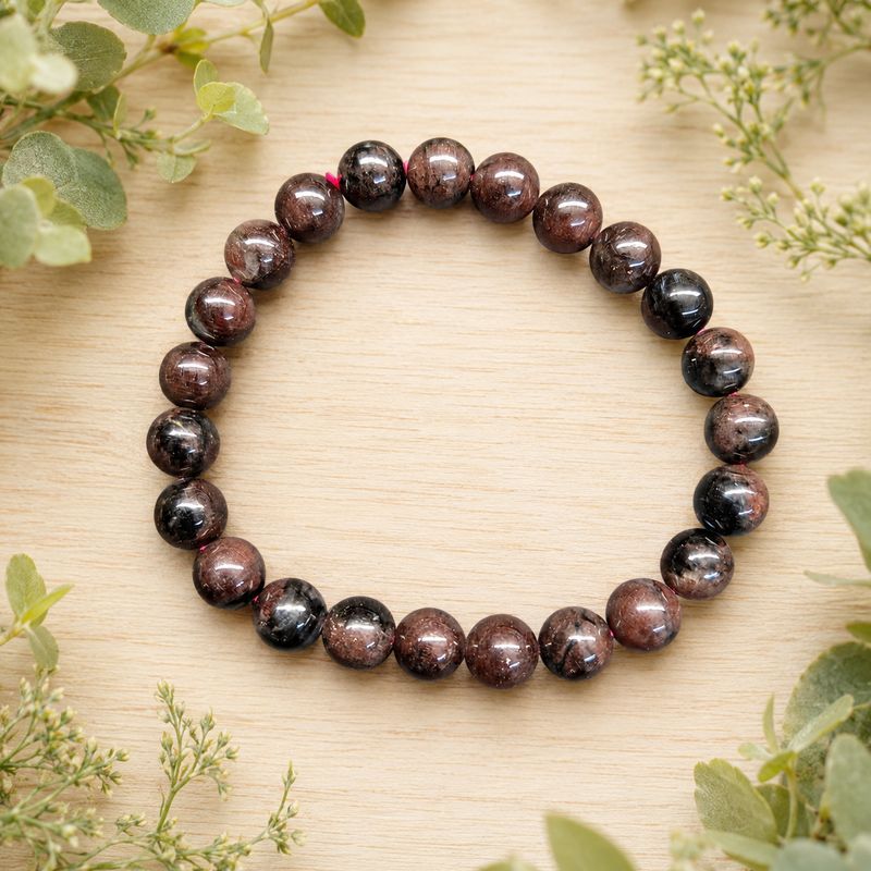 Astrophyllite with Garnet 8mm gemstone bracelet on a light wooden table with greenery.